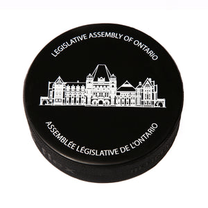Black hockey puck with the imprint of the Legislative Assembly building in white